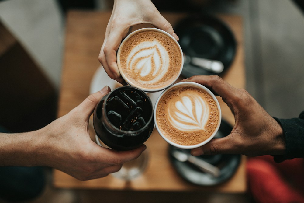 Friends bringing their coffees together over a café table